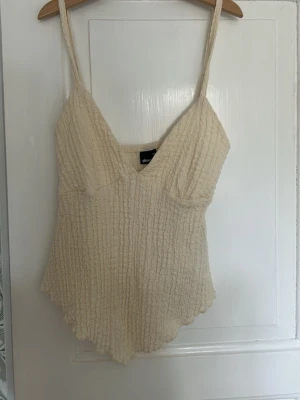 Beige ribbad linnetopp Gina Tricot - Säljer en beige ribbad linnetopp från Gina Tricot i storlek XS. Toppen har smala axelband, v-ringad hals och en lätt vågig nederkant. 