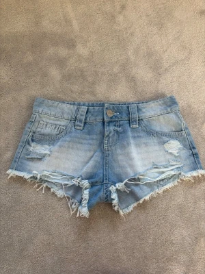 Ljusblå jeansshorts med fransar - Säljer ett par ljusblå jeansshorts med slitna detaljer och fransig kant! Superfina.