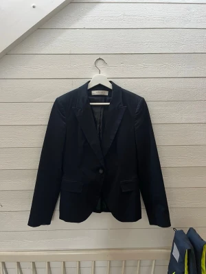 Svart kavaj från Zara Basic - Stilren svart kavaj från Zara Basic med klassisk krage, enkelknäppning och två fickor framtill. Kavajen har en figurnära passform och är helfodrad för extra komfort. Perfekt för en snygg och clean look.