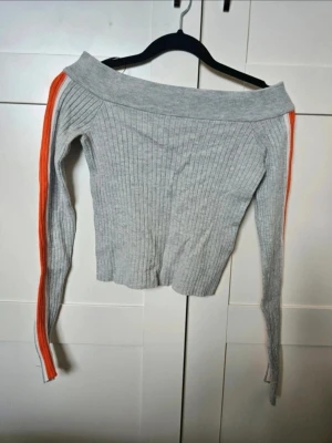 Tröja H&M S - Ribbad offshoulder tröja med ränder  Snygg ribbad stickad tröja i beige med offshoulder-design. Långa ärmar med orange och vit rand längs hela armen ger en sportig vibe. Tröjan är tight och croppad, perfekt att matcha med höga jeans eller kjol.  Kan även hämtas I Partille  E1