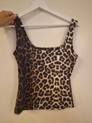 Leopardmönstrat linne - Säljer ett leopardmönstrat linne med breda axelband och rundad urringning. Toppen har en figurnära passform och är perfekt för dig som vill sticka ut med ett djurmönster. Materialet känns mjukt och stretchigt.