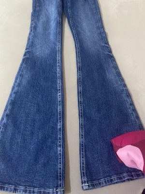 Blåa low wasted boot cut jeans - Säljer ett par blå jeans med utsvängda ben och snygg broderad bakficka med paljettdetaljer. Jeansen har aldrig använts bara provat en gång men då dom inte passade så skäljer jag dom