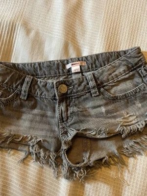 Grå fransiga jeansshorts Gina Tricot - Säljer ett par grå jeansshorts från Gina Tricot  med fransig kant och slitna detaljer. Shortsen har broderade bakfickor med små nitar och klassisk femficksmodell. Inköpta i sommar och använda ett fåtal gånger.