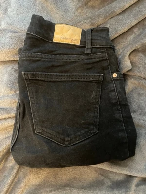 Svarta boot cut jeans från Gina Tricot - Säljer ett par svarta boot cut jeans från Gina Tricot, modellen Perfect Jeans. Jeansen har klassisk femficksdesign, hög midja och smal passform. Materialet är stretchigt för extra komfort och de har bälteshällor samt knappgylf.