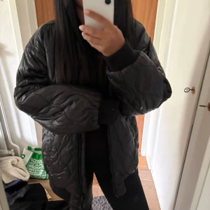 Svart oversized pufferjacka - Säljer en svart oversized pufferjacka med quiltat mönster och breda ärmar. Jackan har en hög krage och två stora fickor framtill. Perfekt för kalla dagar och ger en riktigt chill vibe till din outfit.