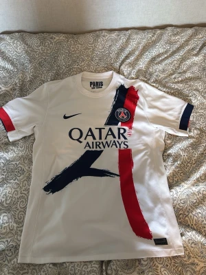 Vit PSG matchtröja Nike Player Edition M - Säljer en vit PSG matchtröja från Nike med blå och röda penseldrag på framsidan. Tröjan har klubbmärke och Qatar Airways-tryck på bröstet samt mörkblå och röda detaljer på ärmarna. Perfekt för fotbollsfans som vill sticka ut på planen.