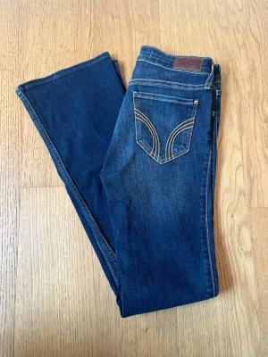 Mörkblå bootcut jeans Hollister - Snygga mörkblå bootcut jeans från Hollister med klassiska kontrastsömmar och broderad bakficka. Modellen är mid-rise och har stretchigt material för extra komfort. Perfekta till sneakers eller boots.