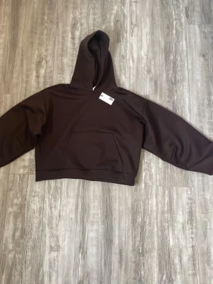 Helt ny brun hoodie med huva från lager 157 - Säljer en stilren brun croppad hoodie med stor huva och magficka. Materialet känns mjukt och bekvämt. Säljer hoodien för att den inte passar, aldrig använd! Original pris: 250