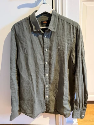 Grön Morris skjorta i linnematerial  - Snygg grön skjorta i linne med klassisk krage och vita knappar framtill. Skjortan har lång ärm och en liten broderad logga på bröstet. Perfekt för dig som letar efter något tunnare i bra material.