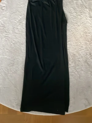 Svart långklänning med slits - En stilren svart långkjol med öppning  på sidan. Kjolen har en enkel och elegant design, perfekt för dig som gillar minimalistisk stil. Tillverkad i ett mjukt och följsamt material som ger en snygg siluett.