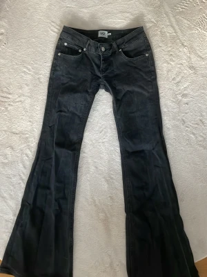 Svarta bootcut jeans med låg midja - Säljer ett par svarta bootcut jeans med låg midja och fem fickor. Jeansen har utsvängda ben och klassisk knappgylf. Perfekta för dig som gillar retrostil och vill ha ett par riktigt snygga jeans i garderoben.