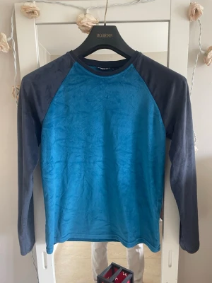Blå långärmad tröja med svarta ärmar - Träningsshirt i polyester, elastan och lycra med blå framsida och mörka ärmar. Snyggt raglansnitt med sportig känsla.