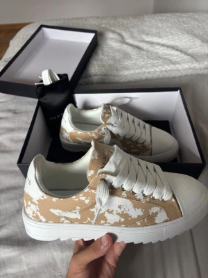 Numeris beige vit - Snygga Numeris sneakers i beige och vitt med unikt mönster. Skorna har bred vit sula, vita skosnören och tåparti i vitt läder. Ovandelen är i textil med beige och vit färgkombination. Perfekta för dig som vill sticka ut med din stil.