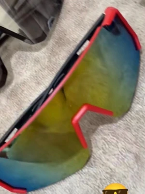 Sportiga solglasögon med spegelglas - Säljer ett par sportiga solglasögon med stora spegelglas i gul och blå ton. Bågarna är svarta med röda detaljer och har en futuristisk, kantig form. Perfekta för dig som vill sticka ut och skydda ögonen mot solen.