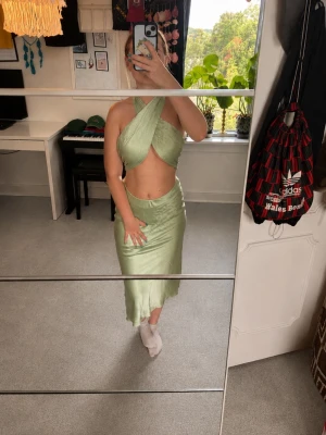 Ljusgrönt set i satin - Snygg ljusgrönt sett i satin med midikjol och korsad halterneck topp. Perfekt för sommarens alla tillfällen och ger en riktigt trendig vibe. Den är från Nelly ur Bianca Ingrossos kollektion. Båda delarna har en del tråddragningar (se exempel på bilderna), men inget som syns på långt håll. Toppen saknar också en knapp (se bild), men ingenting som märks.