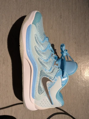 Ljusblå Nike sneakers med vit sula - Säljer ett par snygga ljusblå Nike sneakers med vit sula och silverfärgad swoosh. Ovandelen är i mesh och syntetmaterial med coola detaljer och mönster. Skorna har klassisk snörning och låg profil som ger en sportig vibe. Storlek 41. Tyvärr ingen skokartong. 