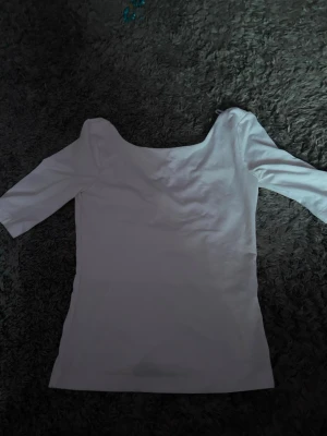 Vit offshoulder topp med trekvartsärm - Säljer en stilren vit offshoulder topp med trekvartsärm. Toppen har en clean look och är tillverkad i ett mjukt material som känns skönt mot huden. Perfekt för dig som gillar minimalistisk stil och vill ha något enkelt men snyggt. Lite öppen rygg och har armbåges längd på ärmarna. Nytt bra skick!!