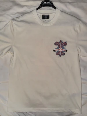 Chrome Hearts t-shirt - Snygg vit t-shirt från Chrome Hearts med ett glittrigt tryck i rött och blått på bröstet. T-shirten har stor-regular passform och rund hals. Perfekt för dig som vill ha något unikt och stilrent i garderoben. Skriv för mer detaljer eller bilder