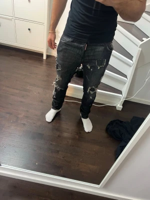 Svarta slitna dsquared jeans - Säljer ett par svarta jeans med tydliga slitningar och hål på både fram- och baksida. Jeansen har en smal passform och klassisk femficksdesign. Perfekta för dig som gillar en edgy och trendig stil.