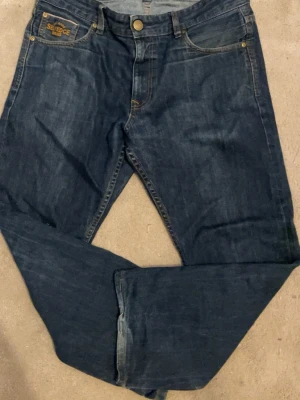 Mörkblå raka jeans med kontrastsömmar - Snygga mörkblå jeans i rak modell med klassiska fem fickor och kontrastsömmar. Jeansen har en patch på fickan där det står 'Selvedge' och dekorativa sömmar på bakfickorna. Tillverkade i slitstark denim, perfekta till vardagslooken.