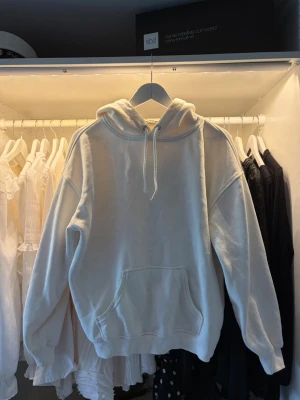 Vit oversized hoodie med huva - Säljer en vit hoodie med stor ficka framtill och dragsko i huvan. Hoodien har långa ärmar och ribbade muddar vid ärmslut och nederkant. Perfekt för en chill och avslappnad stil.