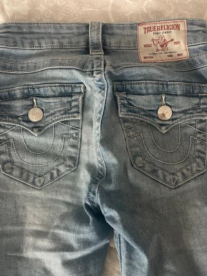 Ljusblå bootcut jeans True Religion - Jeans från true religion. De är i fint skick men det något trassel där nere, se bilden. De är långa för sin storlek men något tighta men stretchiga. Passar om du är en xs/s Skriv för fler bilder eller info 💕