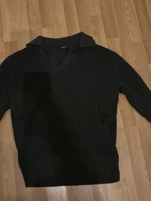 Mörkgrön stickad tröja Massimo Dutti - Snygg mörkgrön stickad tröja från Massimo Dutti i 100% bomull. Tröjan har en krage och v-ringning, samt ribbstickade detaljer vid ärmslut och nederkant. Perfekt för dig som gillar stilrena och klassiska plagg.