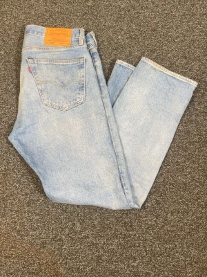 Levi's 501 Light Wash Blue Jeans - Classic Straight Leg, Button Fly - Levi’s 501 Original Fit i ljusblå tvätt. Klassiska jeans med raka ben, knappgylf och den ikoniska röda Levi’s-flärpen på bakfickan.  Fint begagnat skick med snygg naturlig tvätt och lätt vintagekänsla. Inga större skador eller anmärkningar.  📏 Storlek: W31 L30 💙 Skick: 8/10  Perfekta till vardags och enkla att matcha med det mesta.