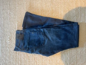 Mörkblå jeans med klassisk passform - Säljer ett par mörkblå jeans från replay med moddelen anbass och med klassisk femficksmodell och normal passform. Jeansen har bälteshällor, knappgylf och är tillverkade i ett mjukt bomullsmaterial. Perfekta till alla typer av outfits!