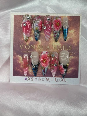 Nerina (XS);Medium Stiletto - Nerina är inspirerad av havets dolda skönhet, där mjuka blommor möter djupa blå toner och skimrande gulddetaljer. Handgjorda press-on naglar i medium stiletto med 3D-blommor, marmoreffekter, reliefer och kristaller. Ett detaljrikt premiumset skapat för dig som vill bära något utöver det vanliga. XS: 14 mm, 11 mm, 11,5 mm, 10 mm, 8 mm