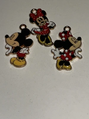 Musse och Mimmi berlocker i emalj - Tre färgglada berlocker i emalj med motiv av Musse Pigg och Mimmi Pigg. Figurerna har detaljer i svart, rött, vitt och gult samt små öglor för att fästa i halsband eller armband. Perfekta för dig som gillar Disney och vill skapa egna smycken.