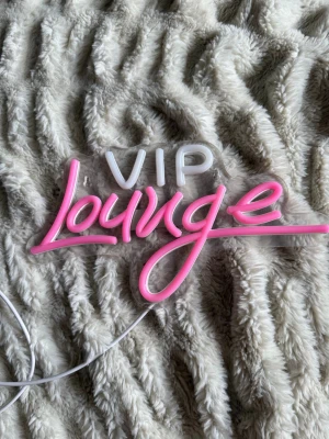 Neonskylt VIP Lounge rosa/vit - Säljer en snygg neonskylt med texten 'VIP Lounge' i vit och rosa. Skylten har USB-sladd och är gjord i plast och LED-material. Perfekt för att ge rummet en cool vibe och skapa loungekänsla.