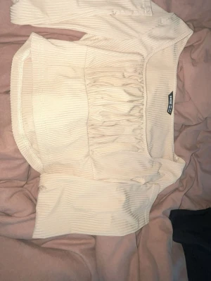 Beige ribbad topp från SHEIN - Trendig beige ribbad topp från SHEIN med korta ärmar och snygg rynkdetalj framtill. Toppen har en fyrkantig urringning och är tillverkad i ett stretchigt material som sitter snyggt på kroppen. Perfekt att styla med jeans eller kjol.