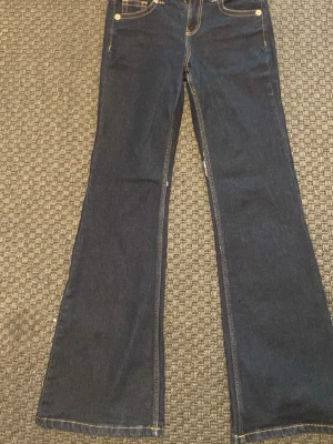 Mörkblå bootcut jeans - Mörkblå bootcut jeans med knappar på bakfickorna. Små trasiga sömmar på båda innerlåren, men inget som märks noga.