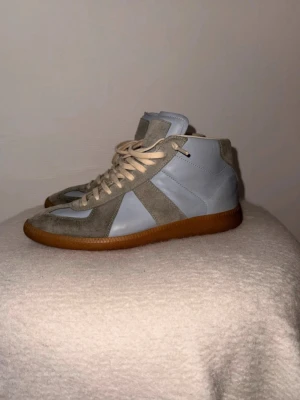 Maison Margiela - Säljer mina gats high i en snygg ljusblå/grå färg. Säljs då dom inte längre kommer till användning.   • Storlek: EU 40 men passar 41 • Skick: 7/10 – använda men fortfarande i bra skick • Material: Läder & mocka  Ingen shoebox tillkommer då den förstördes vid frakt (när jag köpte dom) för cirka 3 år sedan.  Lite slitage finns (se bilder), främst på mocka och insida, men inget som påverkar användning.   Tveka inte att höra av er vid ytterligare information!