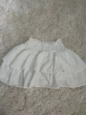 Vit kjol  - Söt vit kjol från Zara med volanger och broderade hål. Kjolen har resår i midjan och är gjord i ett lätt bomullstyg som passar perfekt till varma dagar. Perfekt för dig som gillar en romantisk och somrig stil.🥰