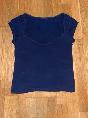 Mörkblå topp med v-ringning - En enkel mörkblå topp med korta ärmar och djup v-ringning. Modellen är figurnära och tyget ser mjukt och stretchigt ut, perfekt för en avslappnad look. Passar till jeans eller kjol för en clean stil.