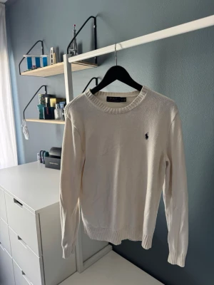 Beige stickad tröja från Polo Ralph Lauren - Klassisk beige stickad tröja från Polo Ralph Lauren med rund halsringning och ribbade muddar. Tröjan har den ikoniska lilla broderade loggan på bröstet och är tillverkad i ett mjukt material som passar perfekt till många olika stilar. Pris kan diskuteras. Kolla gärna in andra plagg på min sida!