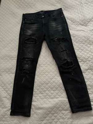 Supply and demand - Säljer ett par svarta jeans med slitningar och hål på både fram- och baksida. Jeansen har skinny fit, fem fickor och coola detaljer som färgstänk och slitna partier. Perfekta för dig som gillar en edgy streetstil.  Storlek XL - passar dig som är 180-186 cm och 70-80kg!!