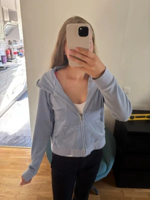 Ljusblå zip hoodie i velour - Säljer en ljusblå hoodie i mjuk velour med dragkedja framtill och fickor på sidorna från Juicy couture. Den har använts max 2 ggr och är som i nytt skick. Etikett storlek är L men den är absolut långt ifrån L, den är som en xs/s!