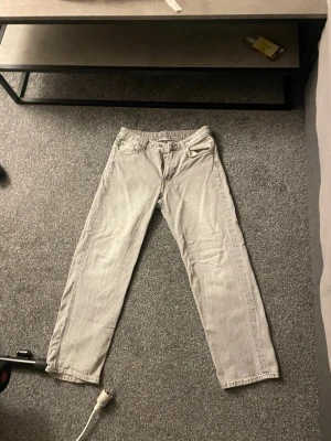 Grå loose fit jeans från H&M - Säljer ett par gråa jeans från H&M med loose fit och raka ben. Jeansen har justerbar midja och klassisk femficksdesign. Perfekta för en avslappnad och trendig stil. Materialet är mjukt denim i bomull.