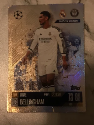 Fotbollssamlarbild Jude Bellingham - Säljer en glittrig samlarbild från Topps med Jude Bellingham i Real Madrid. Kortet har guldfärgade detaljer, Champions League-logga och spelarstatistik. Perfekt för dig som gillar fotboll och samlarbilder.