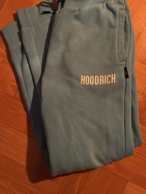 Blåa mjukisbyxor från Hoodrich - Snygga ljusblå mjukisbyxor från Hoodrich med vit logga framtill. Byxorna har resår i midjan med dragsko och sidofickor. Tillverkade i mjukt material som känns skönt mot huden. Perfekta för en avslappnad stil.