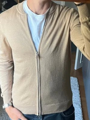 Stenströms zipkofta i beige - stl M - Stenströms zipkofta i beige, storlek M i 100% Merinoull. Personen på bilden är 189cm, väger 78kg.  Använd men i fint skick. Vid dragkedjan är en bristning reparerad, se bild 5. Inga hål eller fläckar i övrigt.  Rök- och djurfritt hem. Skriv gärna om du vill ha fler bilder eller undrar något!