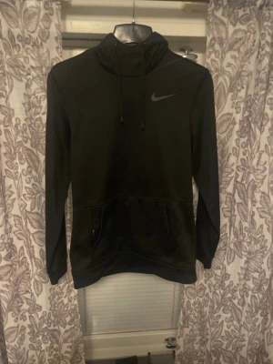 Svart Nike hoodie med huva - Snygg svart hoodie från Nike med klassisk logga på bröstet. Tröjan har huva med dragsko och en stor magficka framtill. Tillverkad i mjukt material och har långa ärmar. Perfekt för en avslappnad och sportig stil.