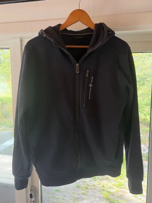 Marin blå hoodie från Sail Racing - Snygg marin blå  hoodie från Sail Racing med dragkedja framtill och en extra bröstficka med zip. Hoodien har huva och diskret logga på bröstet. Perfekt för dig som gillar stilren och sportig look. Materialet känns mjukt och bekvämt. Tröjan är äkta , bevis finns på sista bilden .
