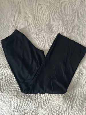 Svarta mjukisbyxor med resårmidja - Ett par svarta byxor med hög midja och stretchigt material. De har en enkel och klassisk design utan synliga detaljer eller mönster. Perfekta att matcha med oversized tröjor eller hoodies för en chill look.