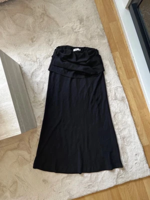 Svart långkjol från Stylein - Säljer en svart långkjol från Stylein med snygg draperad midja. Kjolen har en enkel och stilren design som passar till många olika looks. Materialet känns mjukt och följsamt, perfekt för dig som gillar minimalistisk stil.