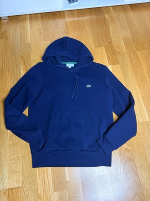 Mörkblå hoodie från Lacoste - Snygg mörkblå hoodie från Lacoste med klassisk krokodillogga på bröstet. Storlek S har även byxorna till den om man är sugen att köpa de med.