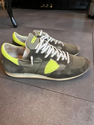Philippe model trpx - Feta Philippe model sneakers i grått med gula detaljer och vita skosnören. Ovandelen är en mix av mocka och textil, med en kontrasterande gul panel på sidan och häl. Klassisk låg modell som passar till många stilar. Lite sliten på hälen.